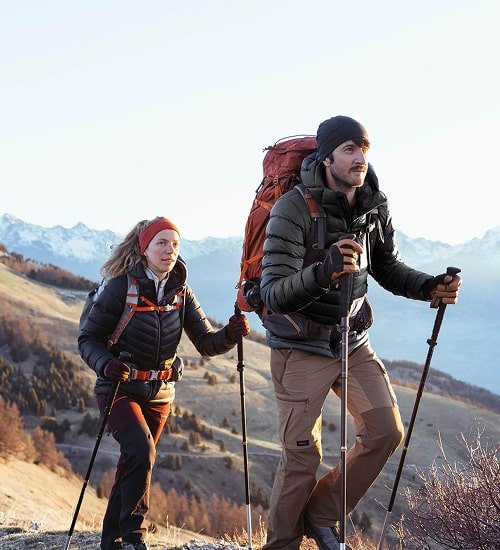 Two hikers with trekking poles and packs on a snowy mountain trail