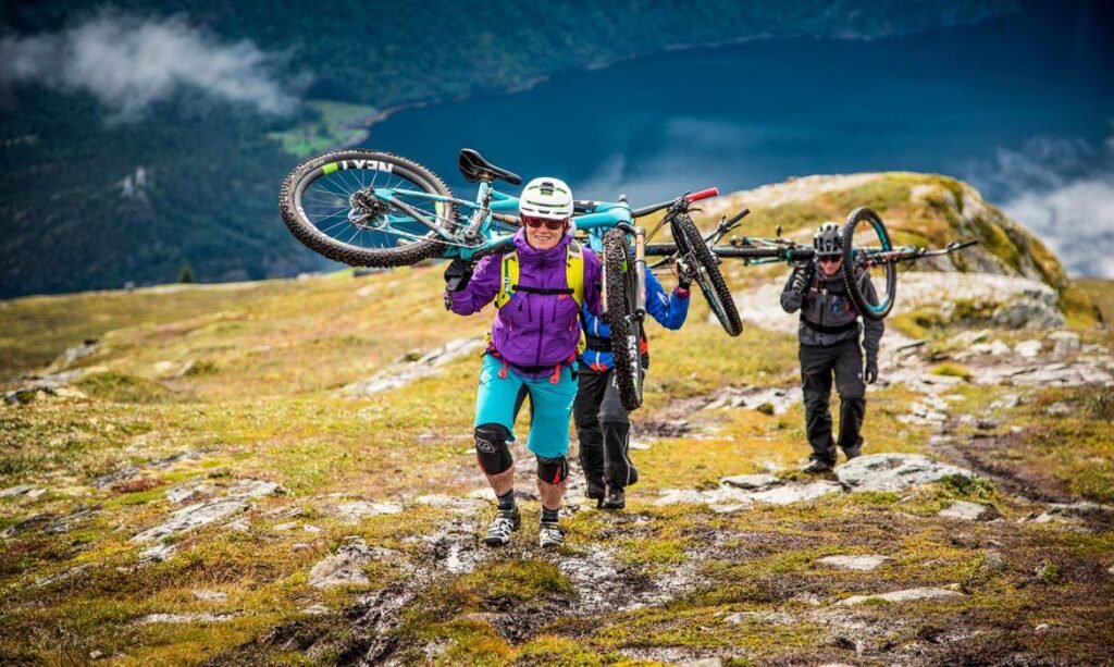 Mountain bikers carrying their bikes up a grassy slope