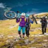 Mountain bikers carrying their bikes up a grassy slope