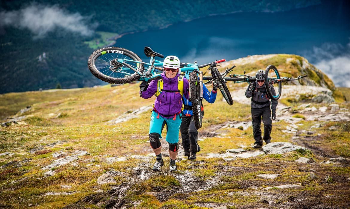 Mountain bikers carrying their bikes up a grassy slope