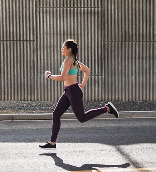 Woman running on a road beside a corrugated metal wall