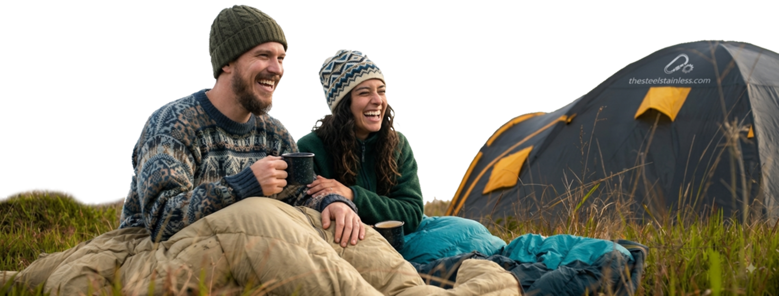 Two campers wrapped in a blanket with hot drinks outside a tent at dusk