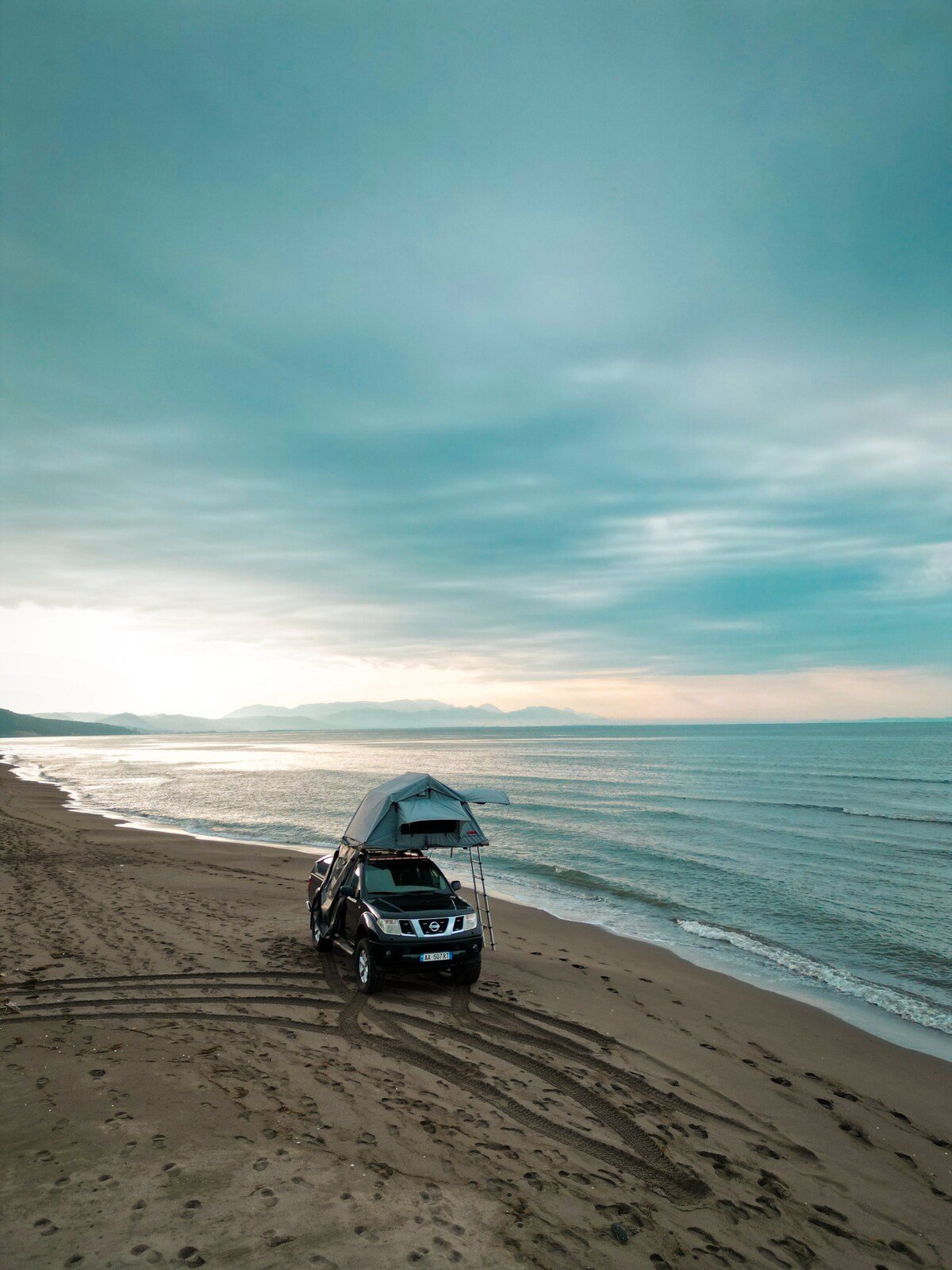 Four wheel drive with a rooftop tent parked on a beach at dusk